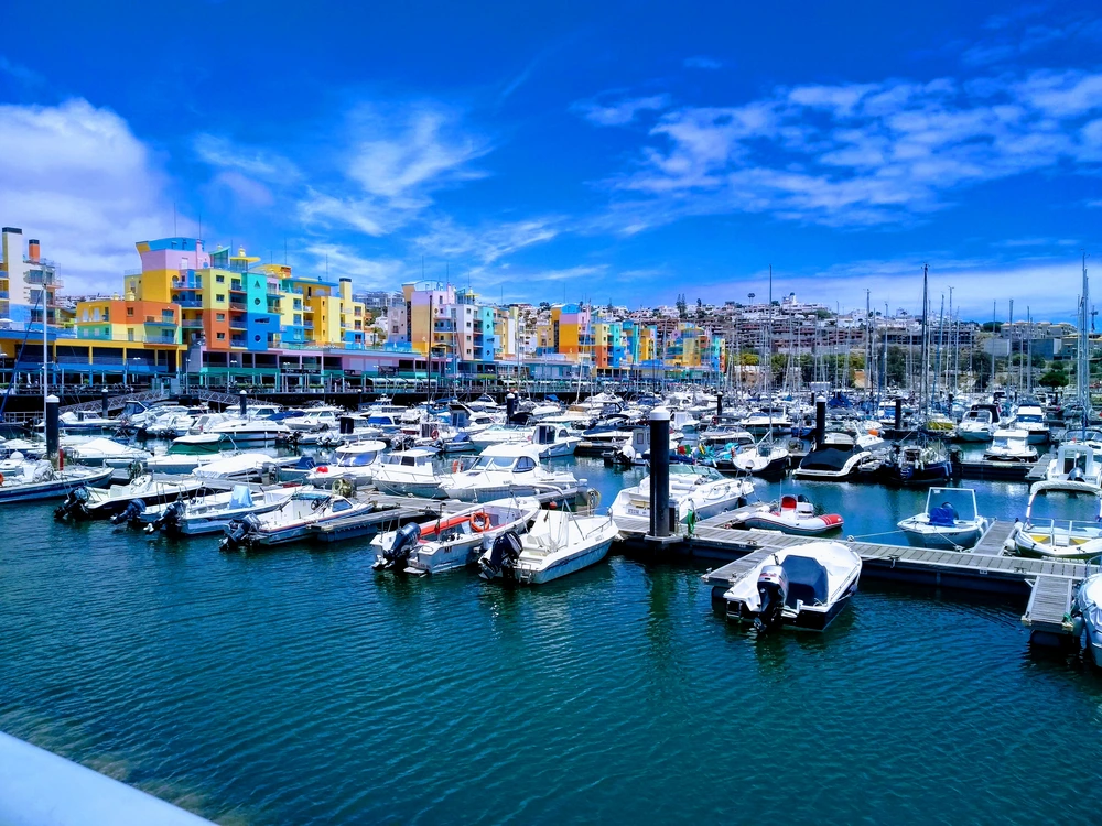 The famous colorful buildings of the Albufeira Marina on a bright sunny day, with many yachts and boats docked in the calm, blue water.