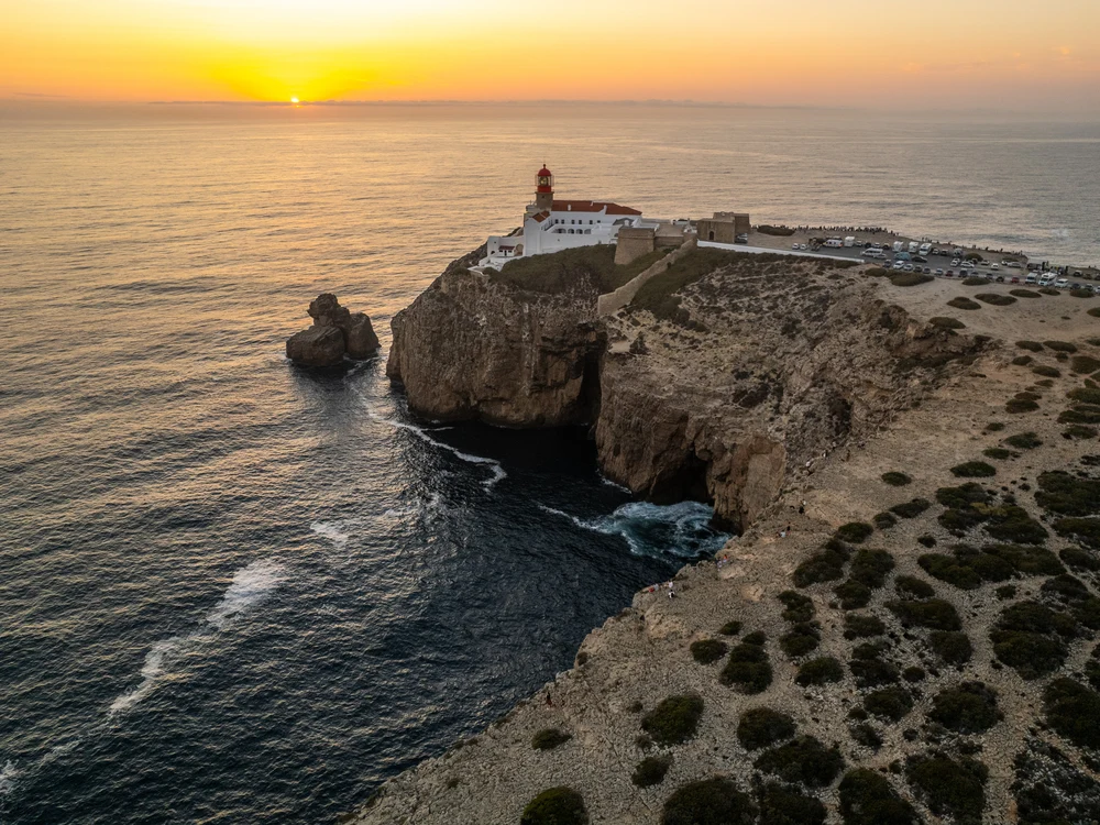 The stunning Cape St. Vincent lighthouse in Sagres, perched on a cliffside as the sun sets over the Atlantic Ocean.