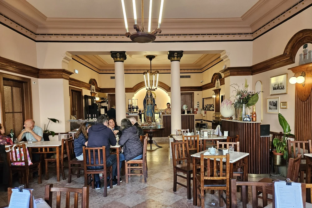 The historic interior of Café Calcinha in Loulé, showing patrons at tables, elegant columns, and a classic European café atmosphere.