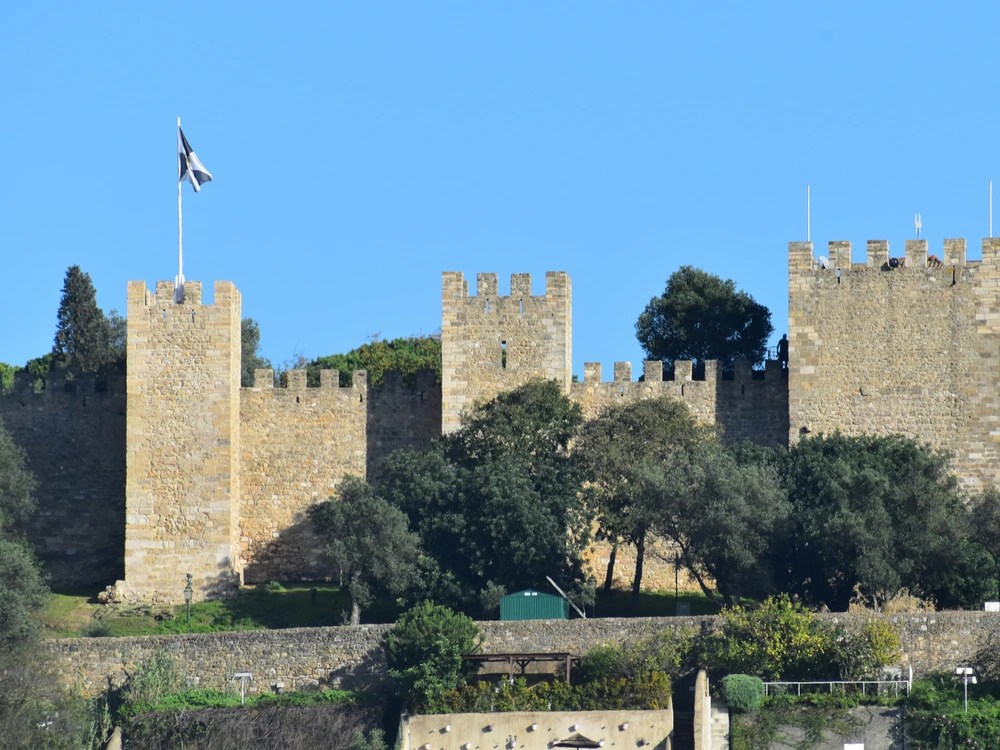The historic stone walls and towers of Castelo de São Jorge (Saint George's Castle) standing tall against a clear blue sky in Lisbon, Portugal.