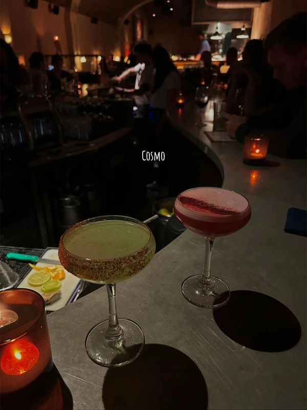 Two colorful cocktails, one green with a seasoned rim and one pink, on the counter at Cosmo, a top cocktail bar in Lisbon.