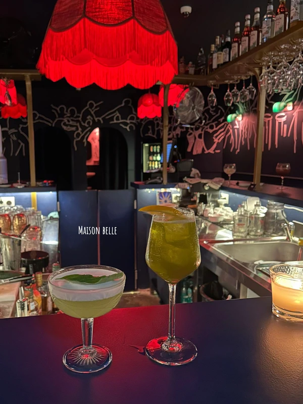 Two expertly crafted green cocktails on the bar at Maison Belle, a stylish cocktail bar with red lighting in Lisbon.