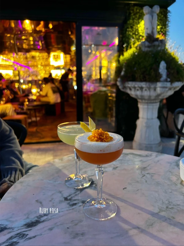 An orange foam cocktail with a flower garnish on a marble table at Ruby Rosa, a rooftop cocktail bar in Lisbon with city views.