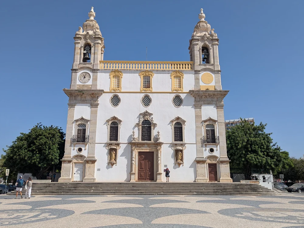 The magnificent Baroque facade of the Igreja do Carmo (Carmo Church) in Faro, with its twin bell towers against a clear blue sky.