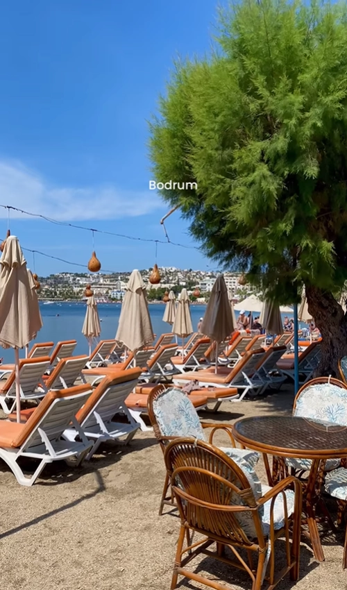 A relaxing beach scene in Bodrum, Turkey, with comfortable lounge chairs and umbrellas on the sand overlooking the Aegean Sea.