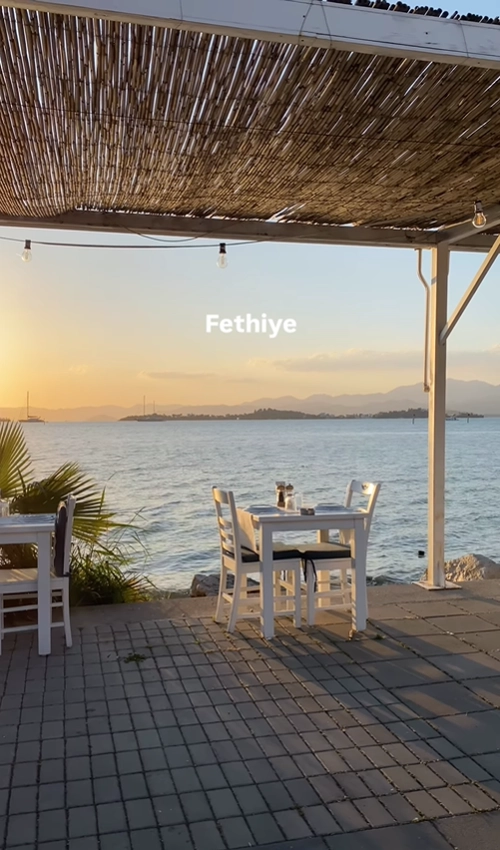 A romantic sunset view from a waterfront restaurant patio in Fethiye, Turkey, overlooking the calm harbor and mountains.