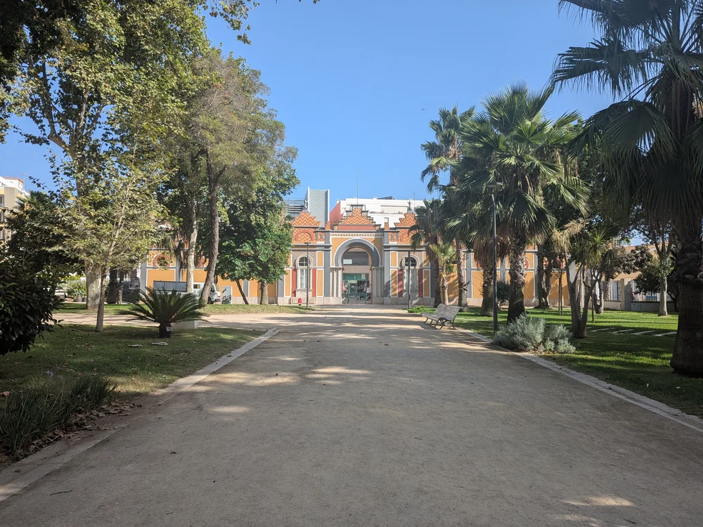 A tranquil path through the lush Jardim da Alameda João de Deus park in Faro, with its iconic main building in the distance.