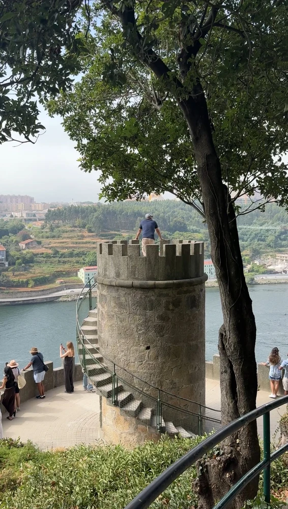 A scenic viewpoint with a stone tower in the Jardins do Palácio de Cristal, offering views of the Douro River in Porto.