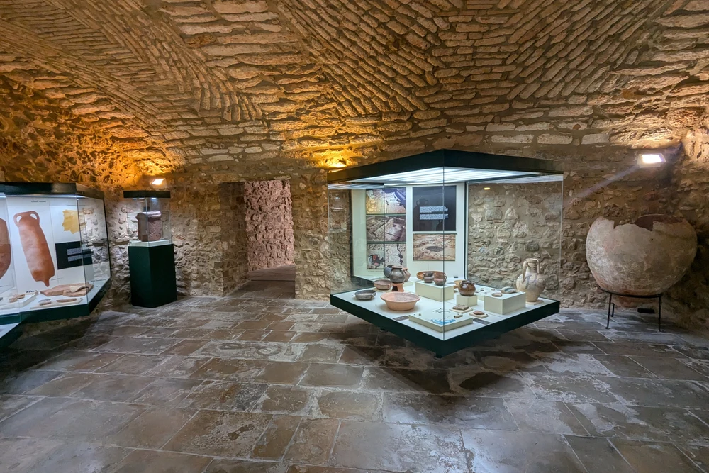 An exhibition room inside the Loulé Municipal Museum, displaying ancient pottery and artifacts in glass cases under a vaulted stone ceiling.