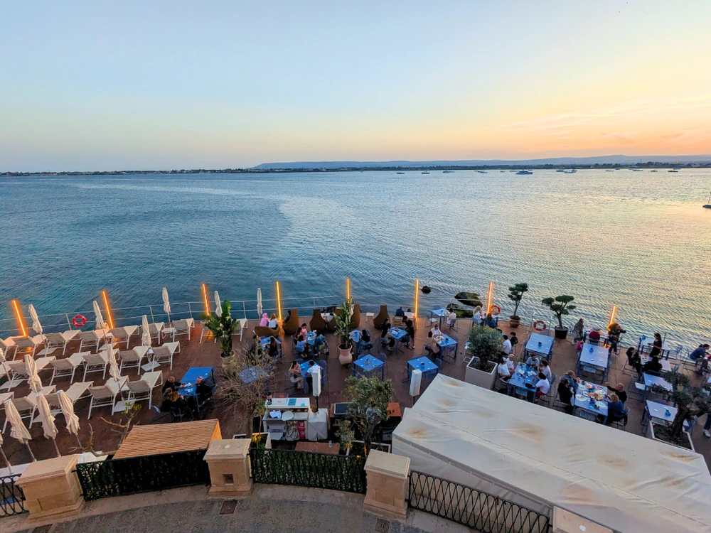 Seaside sunbeds and dining tables at Zefiro Solarium during sunset in Ortigia