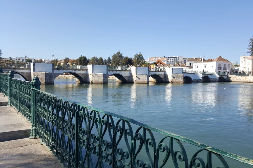The iconic white arches of the Ponte Romana (Gilão River bridge) in the heart of Tavira, with a decorative green railing.