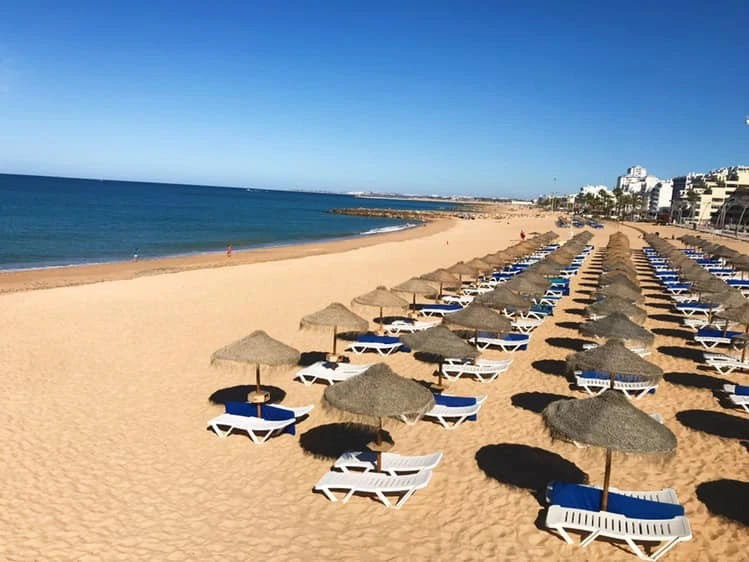 Rows of sunbeds and thatched umbrellas on the golden sands of Praia da Gaivota beach in Quarteira.