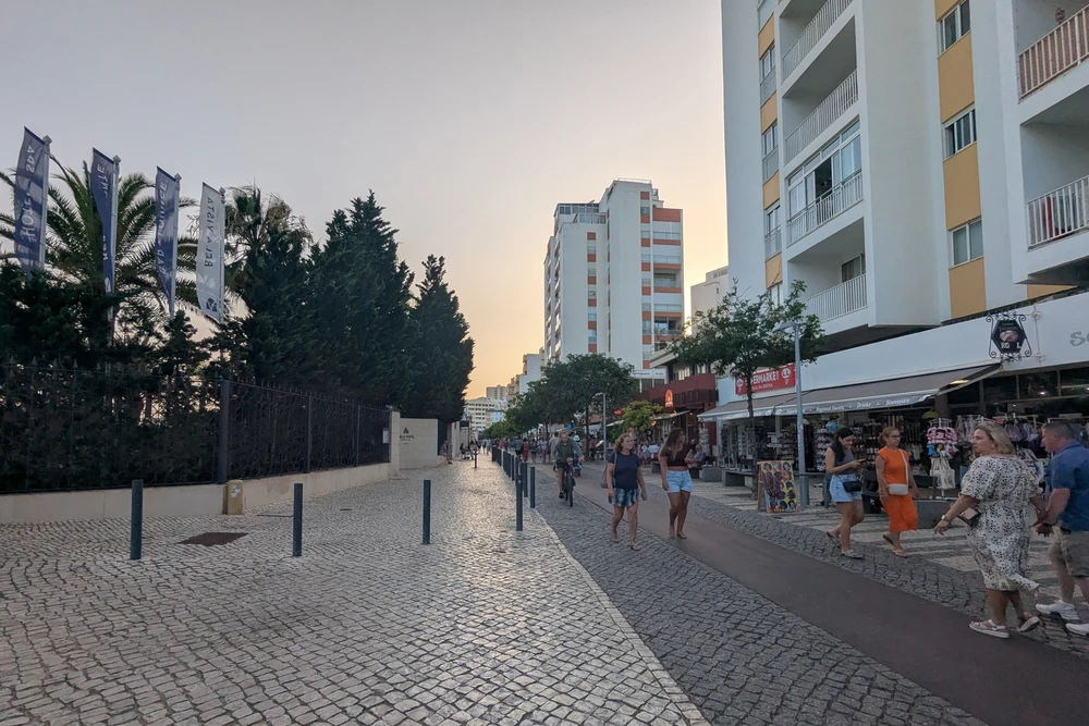 Pedestrian-friendly Avenida Tomás Cabreira in Praia da Rocha lined with shops, cafes, and modern buildings at sunset