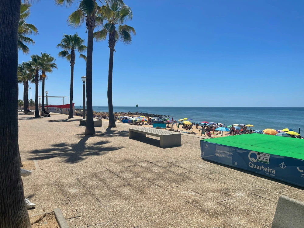 Looking out from the sunny, palm-tree-lined promenade onto the crowded beach and blue ocean in Quarteira.