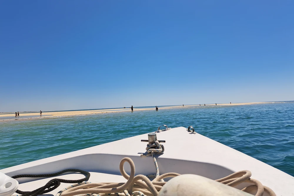 View from a small boat approaching a long, sandy beach or sandbar within the Ria Formosa Natural Park near Olhao, Portugal.