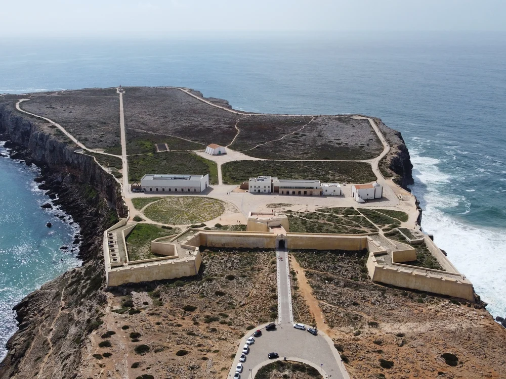 A sweeping aerial view of the historic Sagres Fortress, showcasing its formidable walls and buildings perched on the headland.