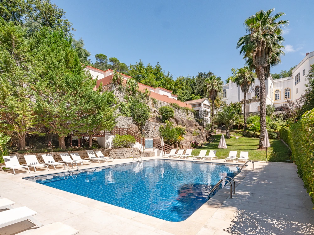 The sunny swimming pool at the Vila Termal das Caldas hotel in Monchique, surrounded by lounge chairs and lush gardens.